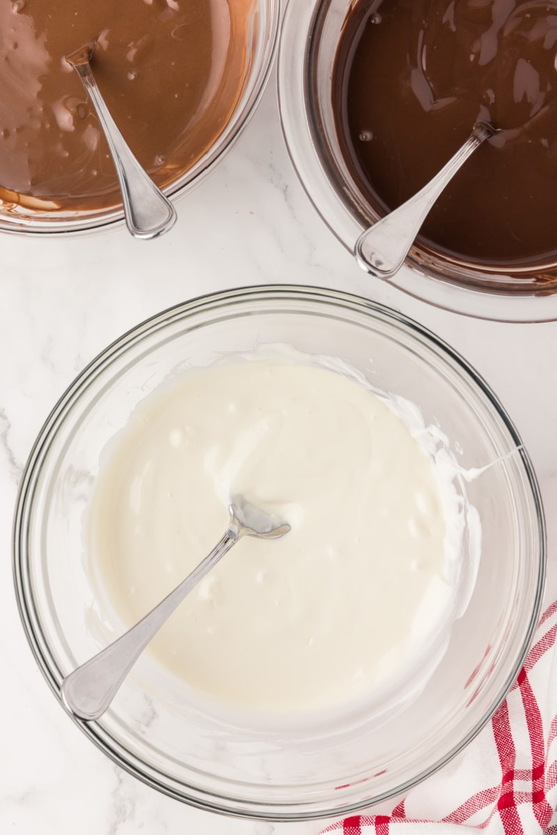 White melted chocolate in a clear glass bowl with a spoon on a white countertop