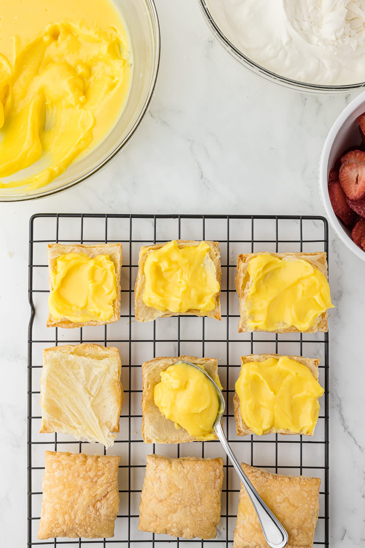 Open square baked puff pastries with yellow custard on top while sitting on a cooling rack