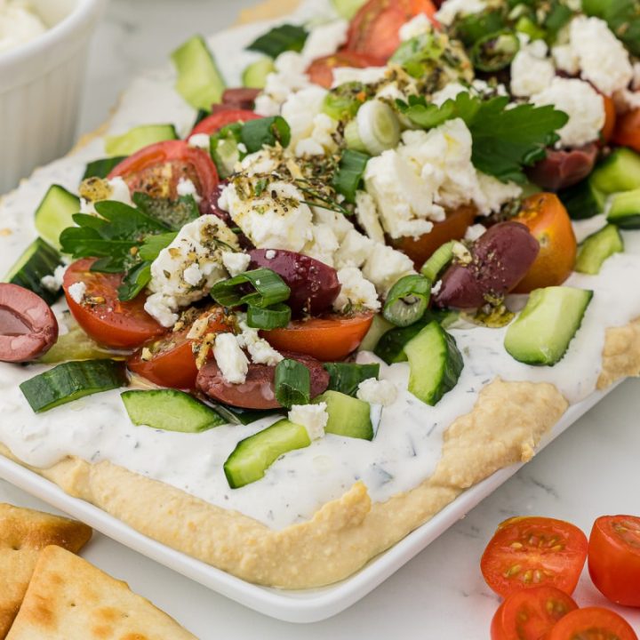 A party tray full of a greek appetizer dip topped with feta cheese with crackers for dipping