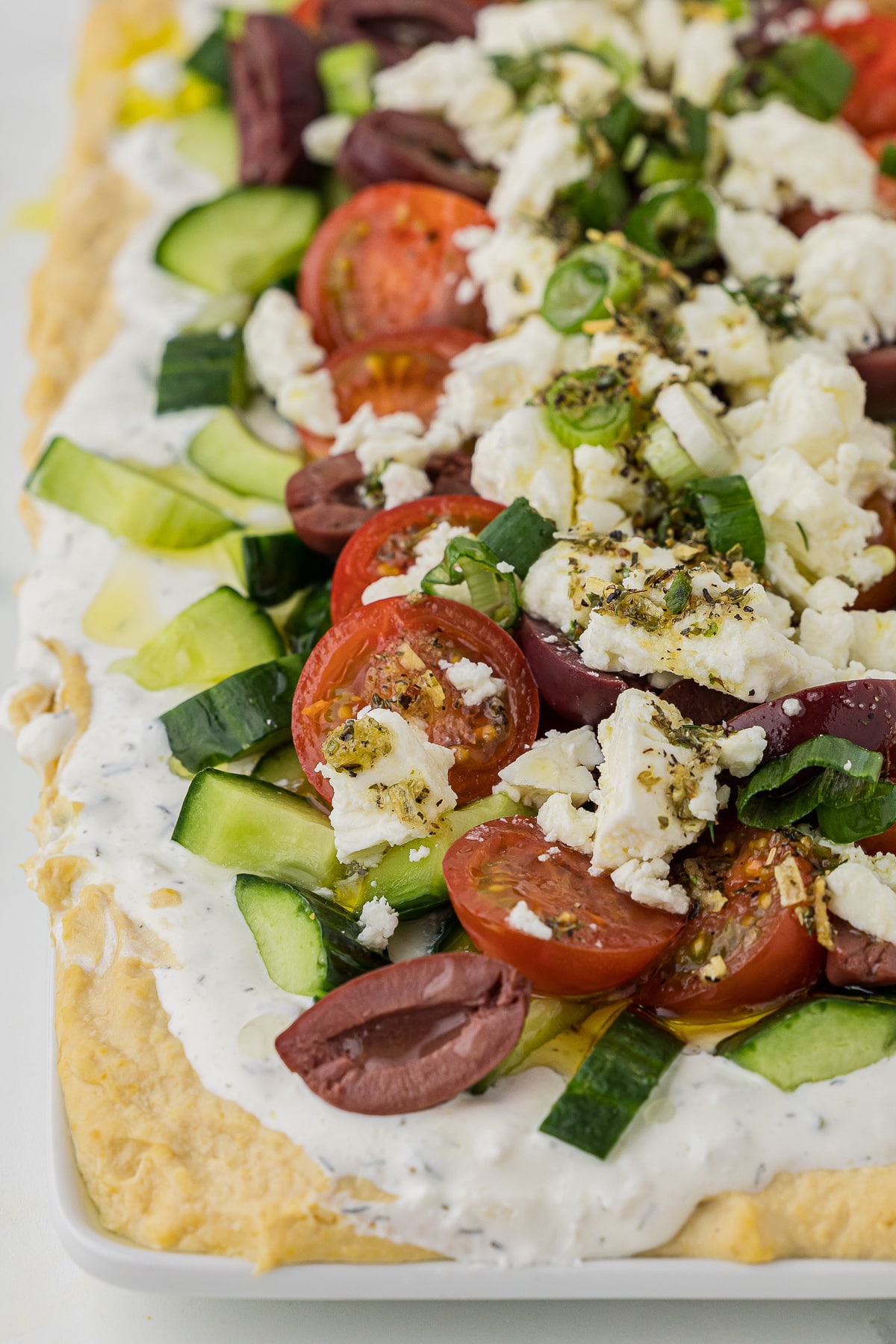 close up shot of a greek party dip appetizer which includes hummus, yogurt and veggies topped with feta cheese
