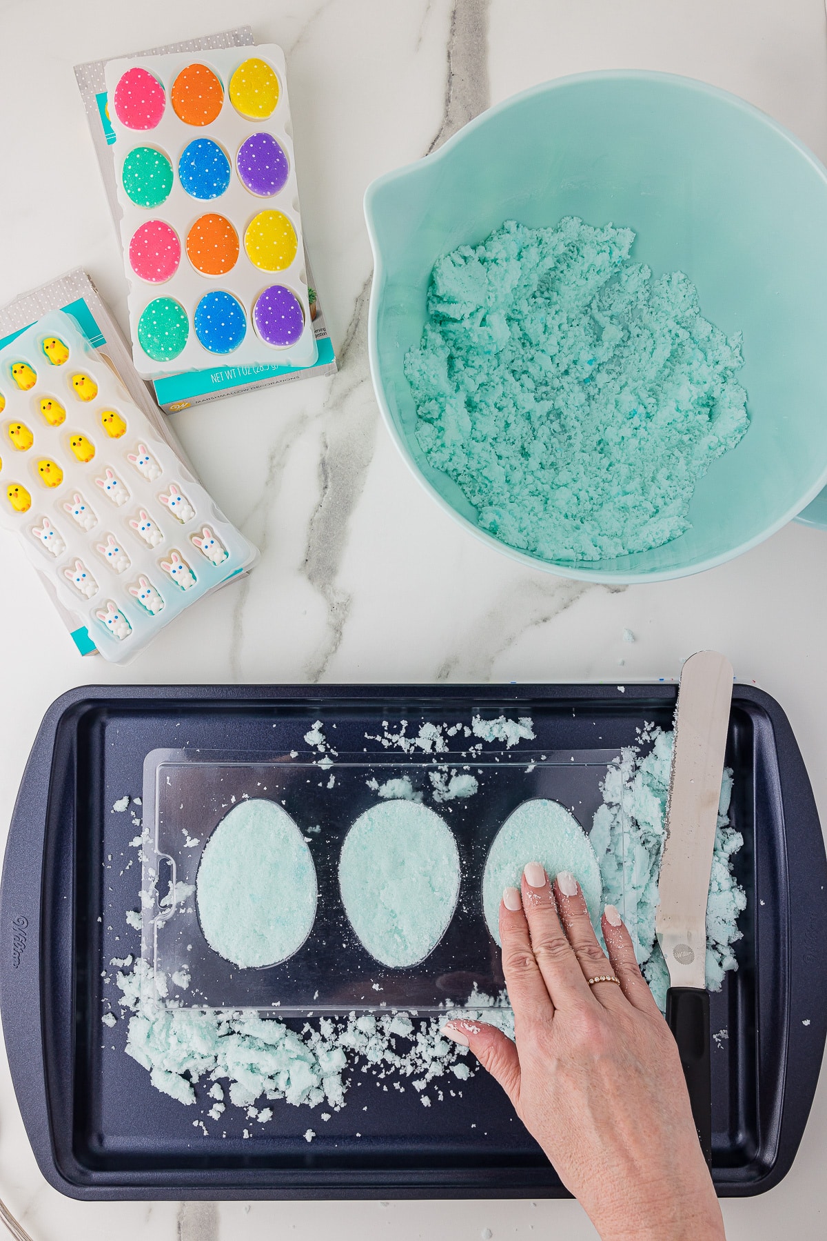 A hand pushing light blue sugar into an Easter Egg mold to make panoramic candy eggs