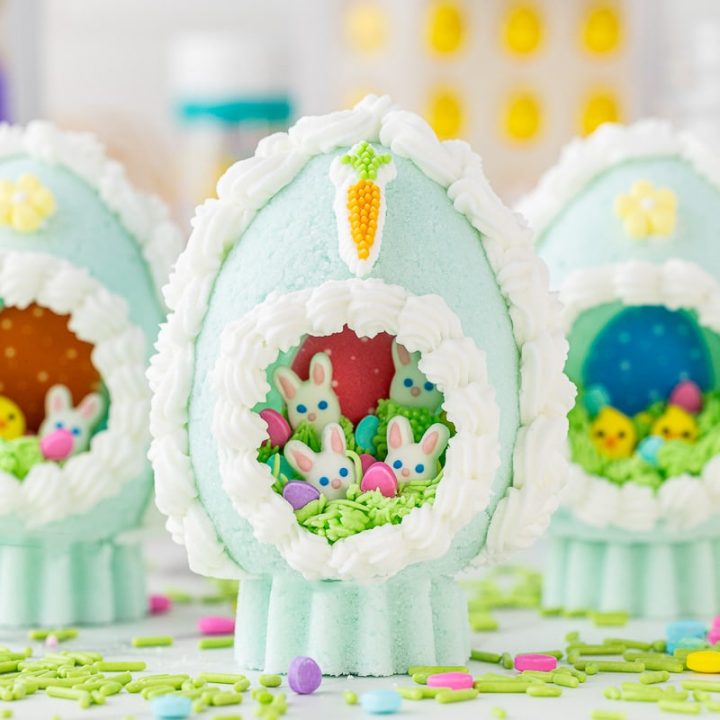 Three panoramic sugar Easter eggs displayed with candy confetti and baking supplies in the background