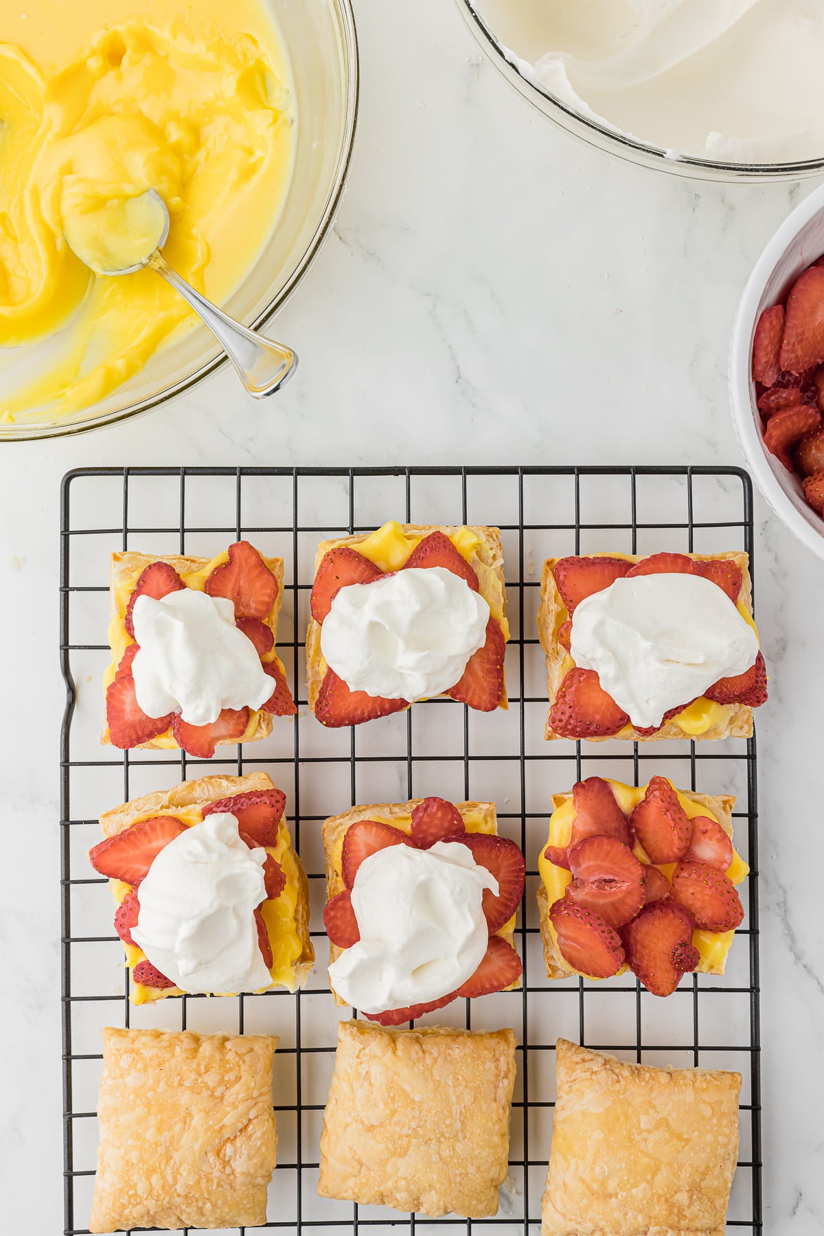 Puff Pastries on a cooling rack with custard and strawberries and whipped topping on them