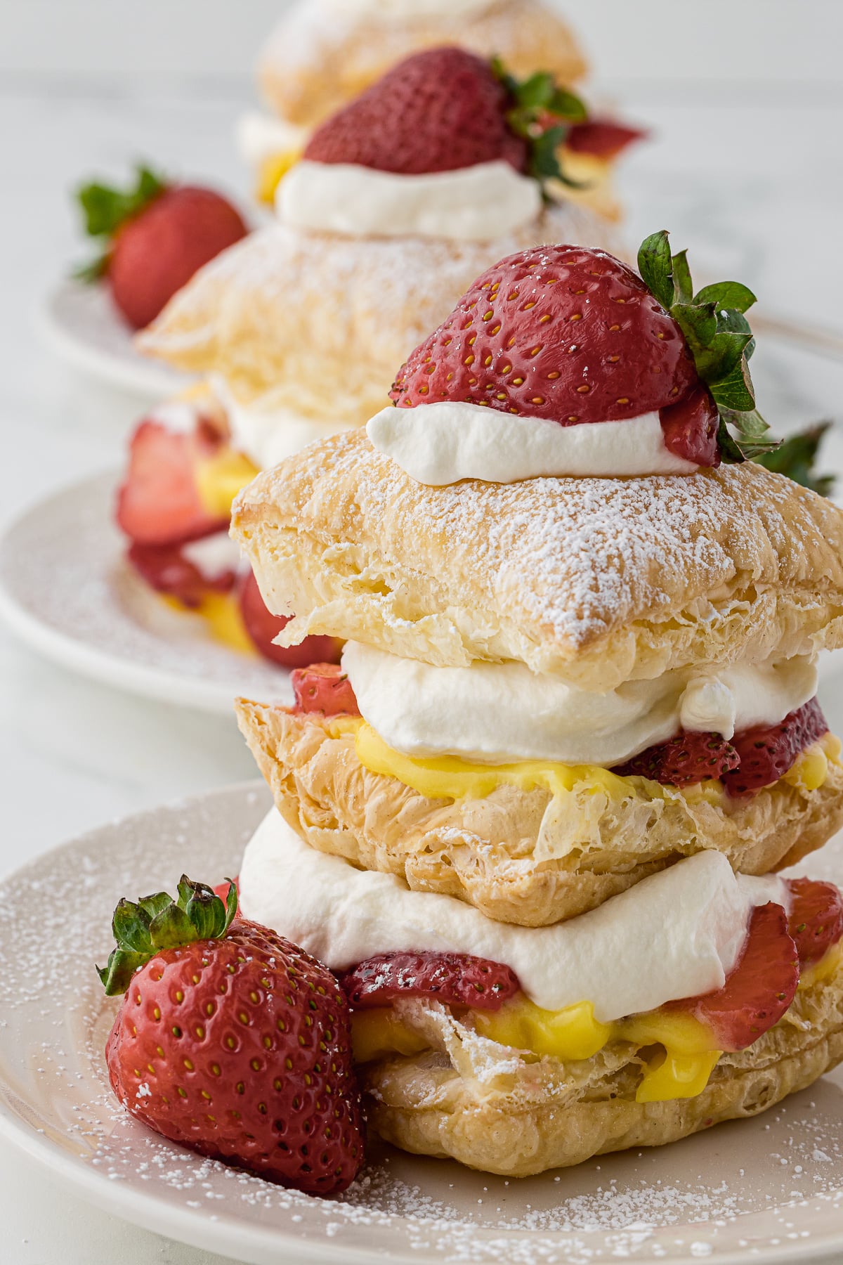Strawberry Napoleon desserts on white plates with fresh strawberries and dusted with powdered sugar