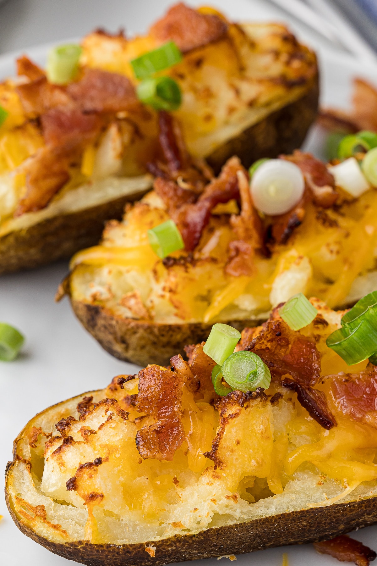 a closeup of 3 twice baked potatoes with melted cheese, bacon bits, and sliced green onions