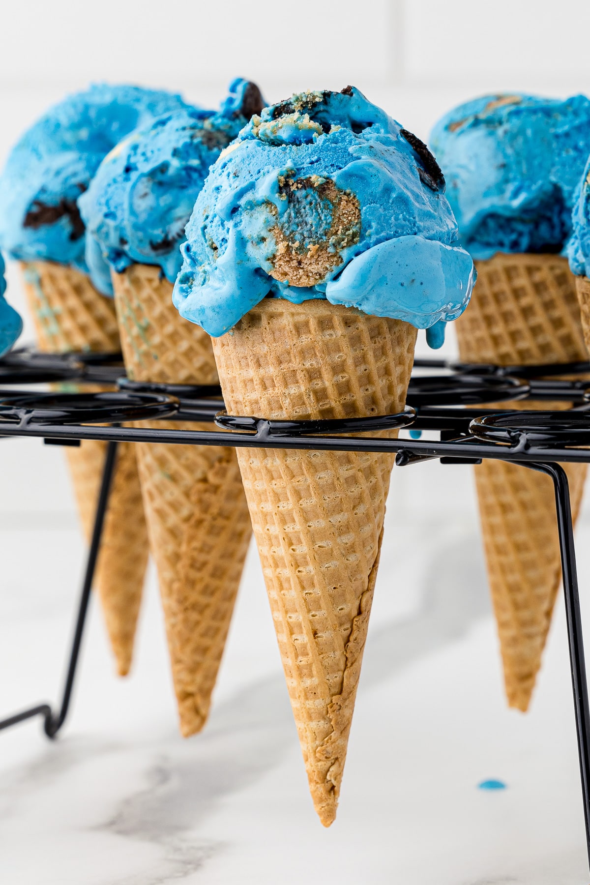 blue ice cream in sugar cones sitting in a black metal ice cream cone holder rack