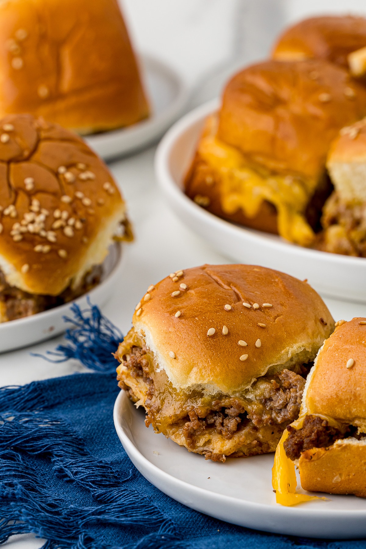 cheeseburger sliders on white plates with a navy blue napkin on a white marble countertop