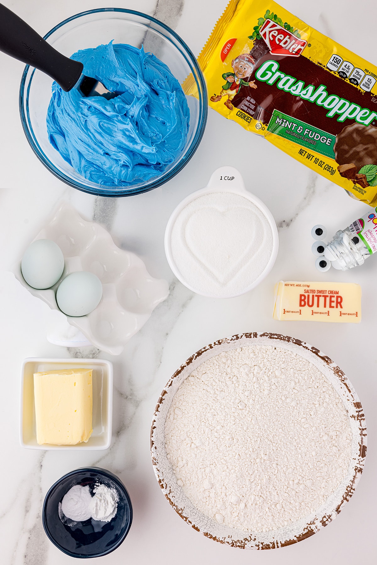 Ingredients for making sugar cookies on a white background including sugar, eggs, butter, flour, and frosting