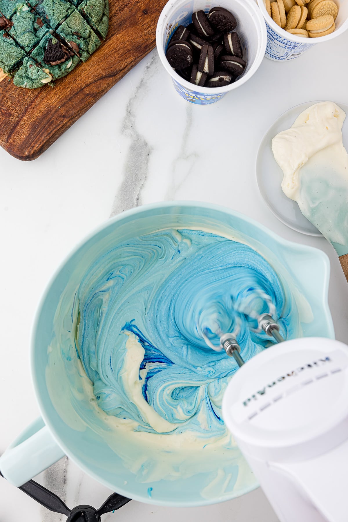 Light blue bowl full of ice cream with added blue food coloring being stirred with an electric mixer