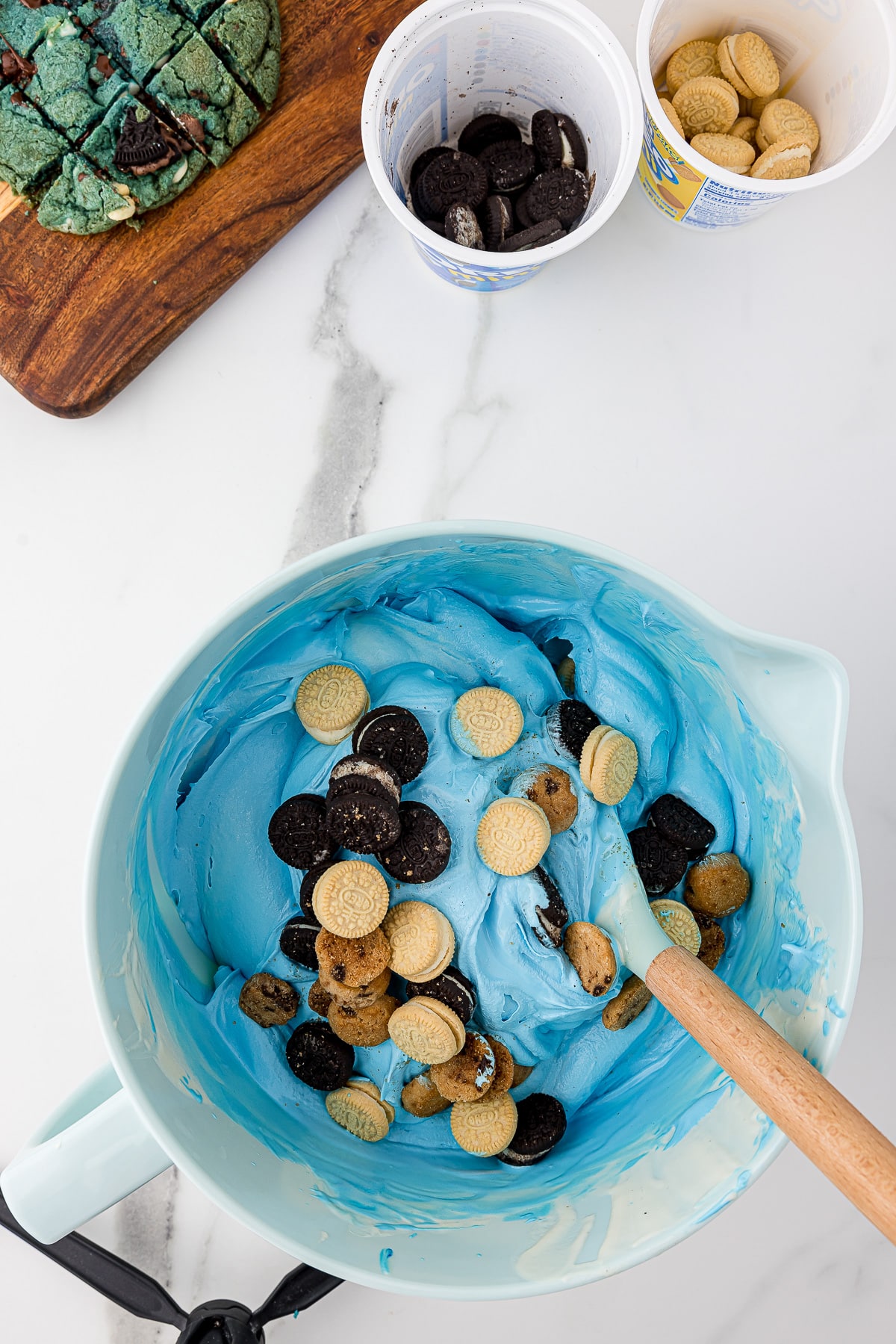 Dropping mini cookies into a blue ice cream mixture in a mixing bowl to make homemade cookie monster blue ice cream