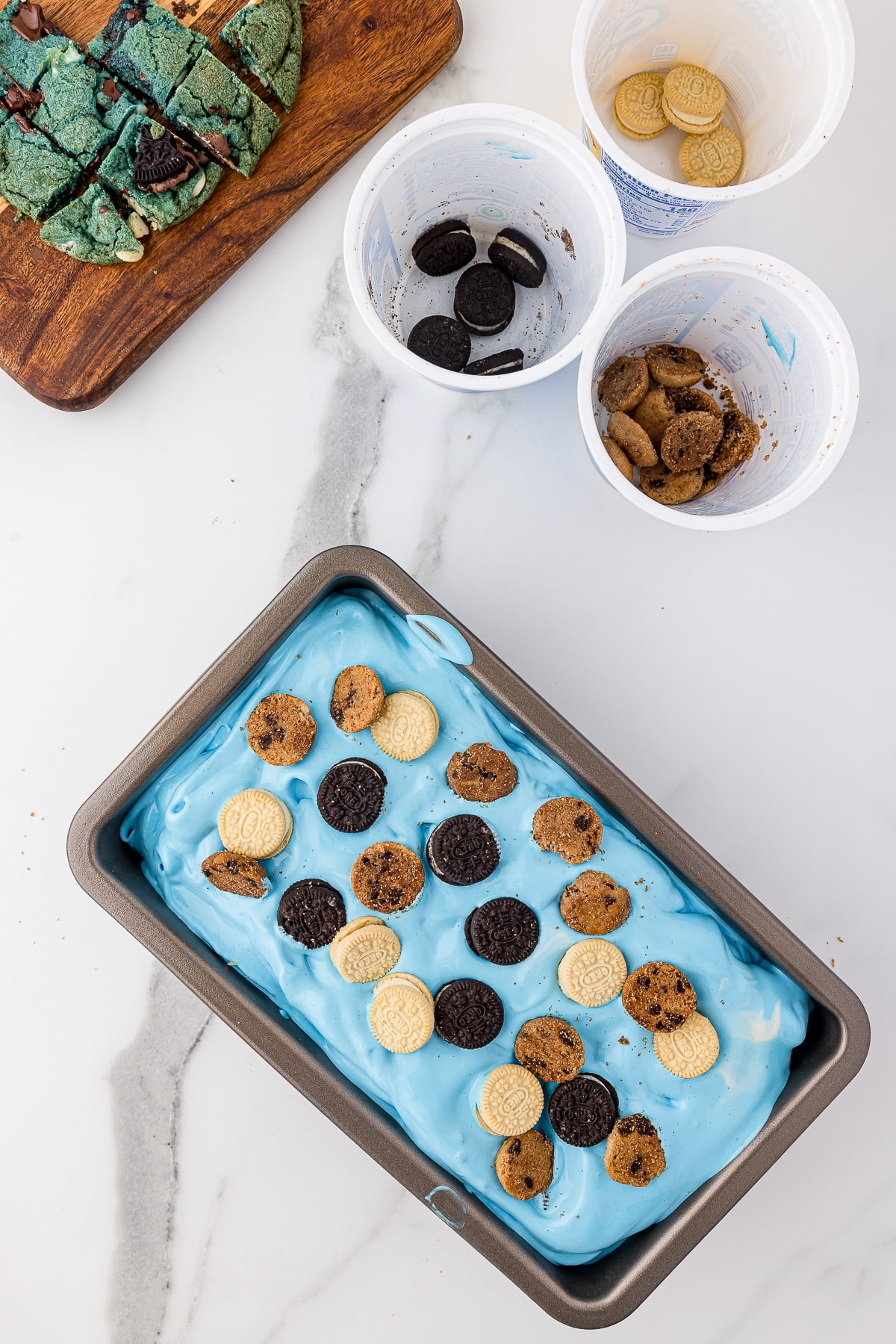 Blue ice cream in a metal bread pan sprinkled with mini chocolate chip and oreo cookies