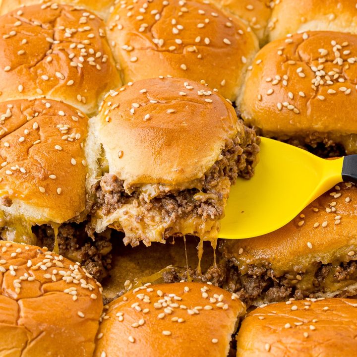 a tray of Hawaiian rolls cheese sliders, one being lifted out of the pan with a yellow spatula