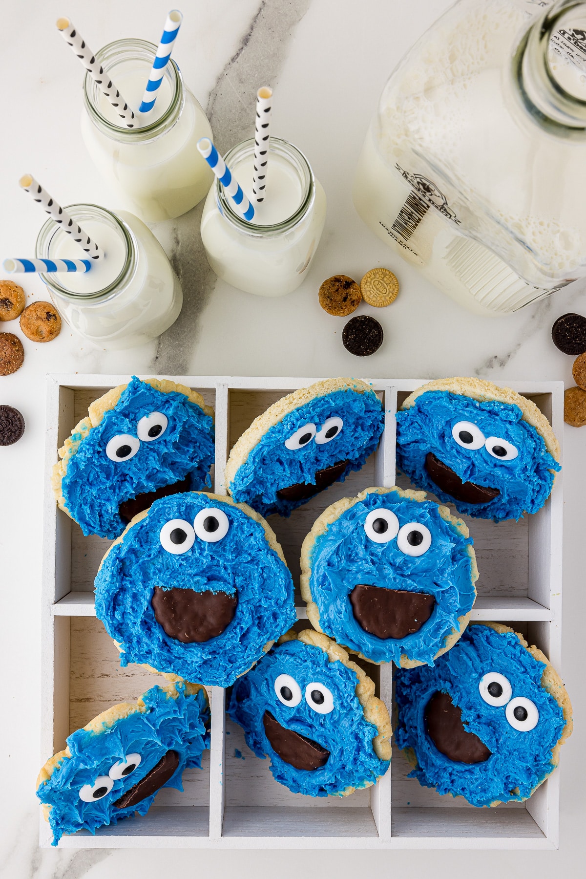 overhead shot of cookie monster themed cookies in a box on a white countertop with milk in the background and mini cookies on the counter