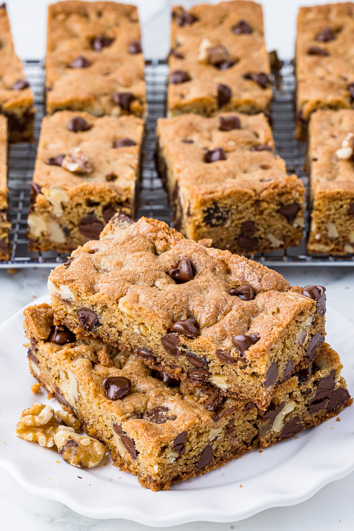 toll house chocolate chip cookie bars on a white plate with more bars on a cooling rack in the background