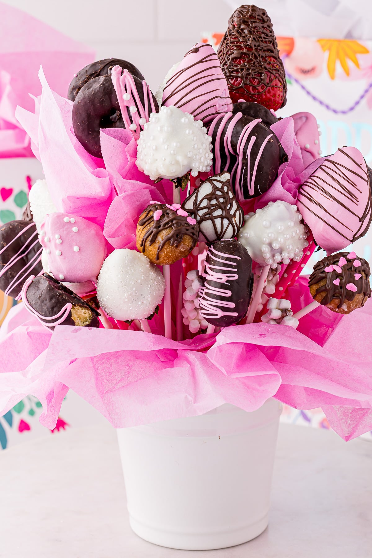 A bright bouquet of chocolate covered treats in pink tissue in a white bucket