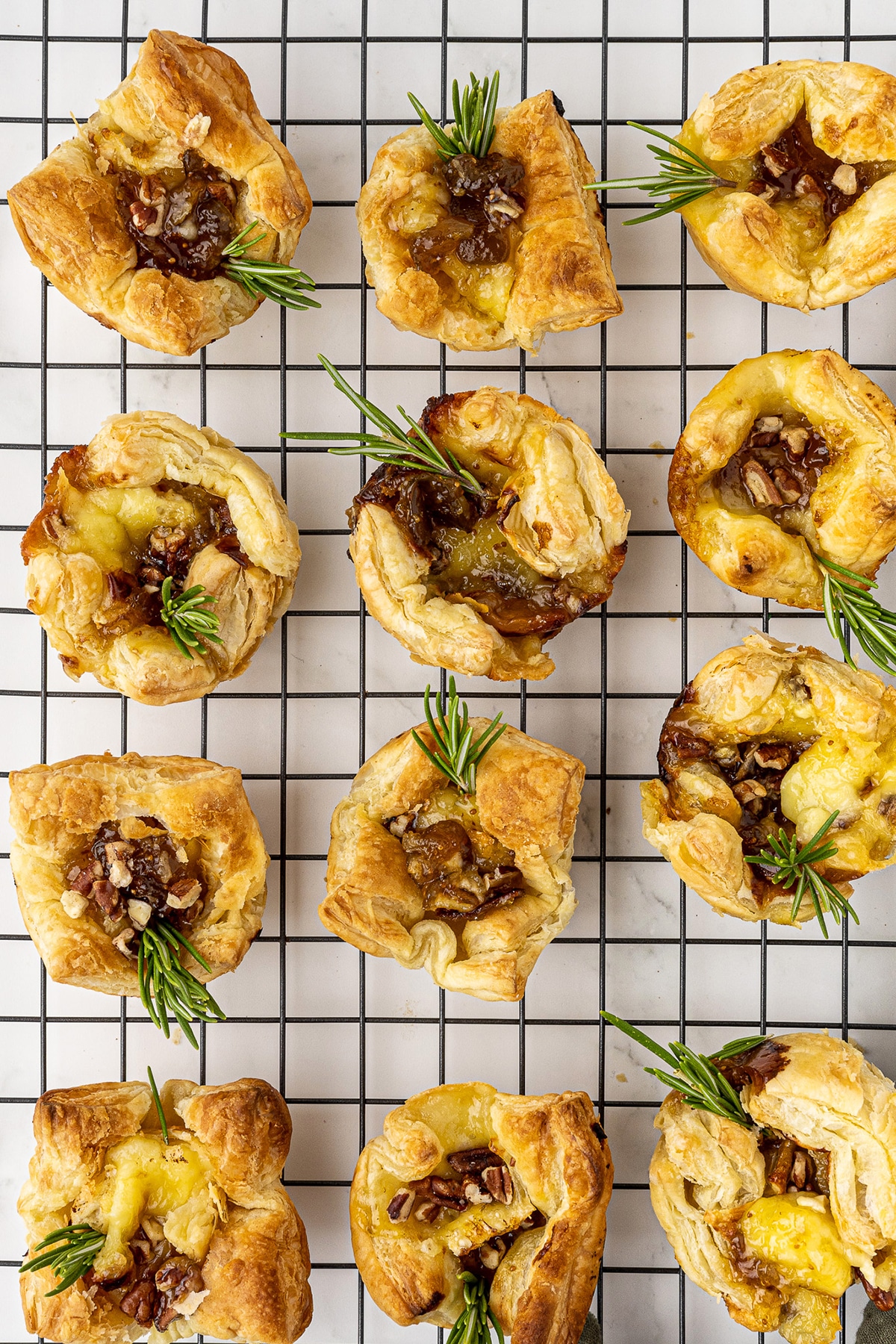 a dozen baked brie bites on a black wire cooling rack that is sitting on a white marble countertop