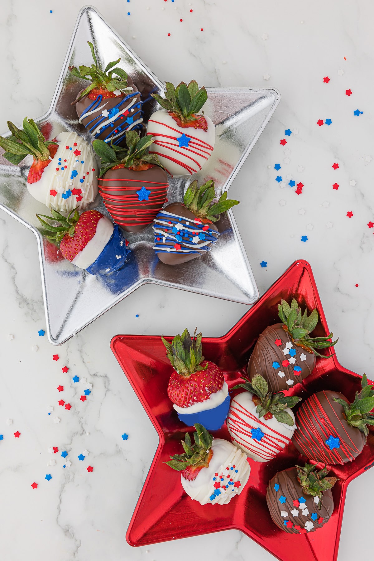 A red star-shaped plate and a silver star-shaped plate, each with 6 strawberries covered in white or dark chocolate and red, white and blue edible sprinkles, stars and stripes.