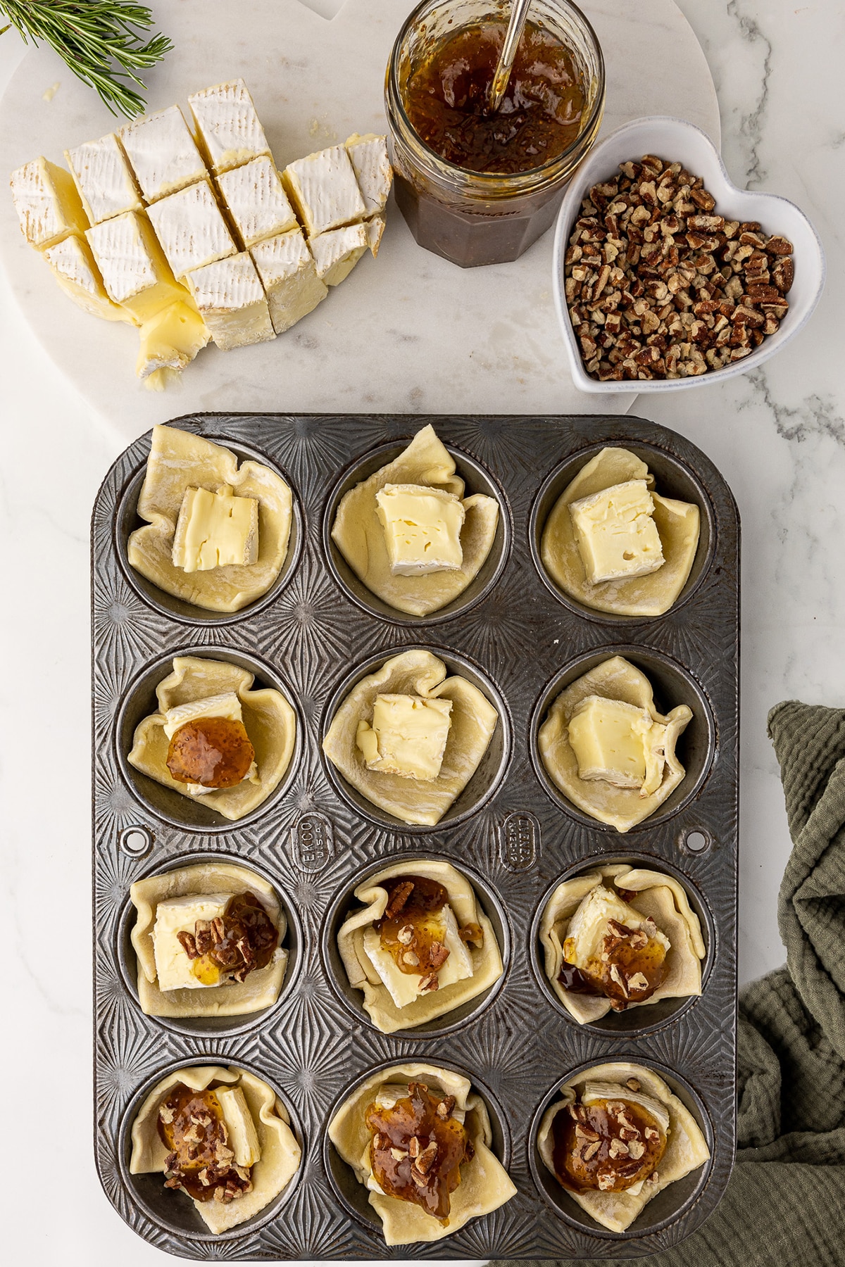antique muffin pan filled with unbaked brie bites, topped with fig jam and walnuts