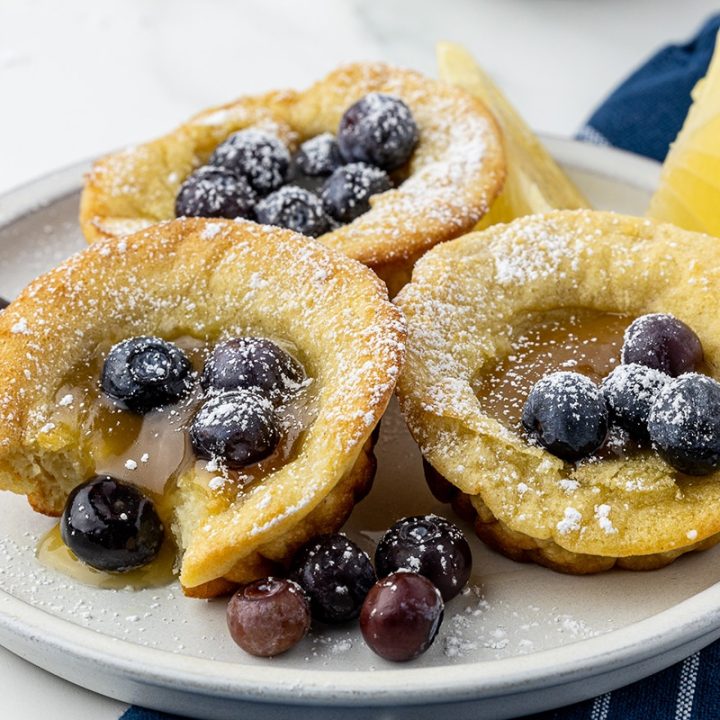 dutch babies on a salad plate with lemon curd, blueberries and lemon slices, on a white countertop and a blue and white napkin under the plate