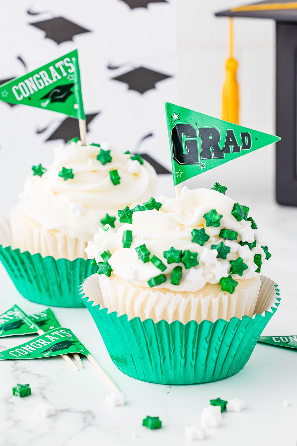 White and green decorated graduation cupcakes featuring graduation and congrats flags with green and white star sprinkles