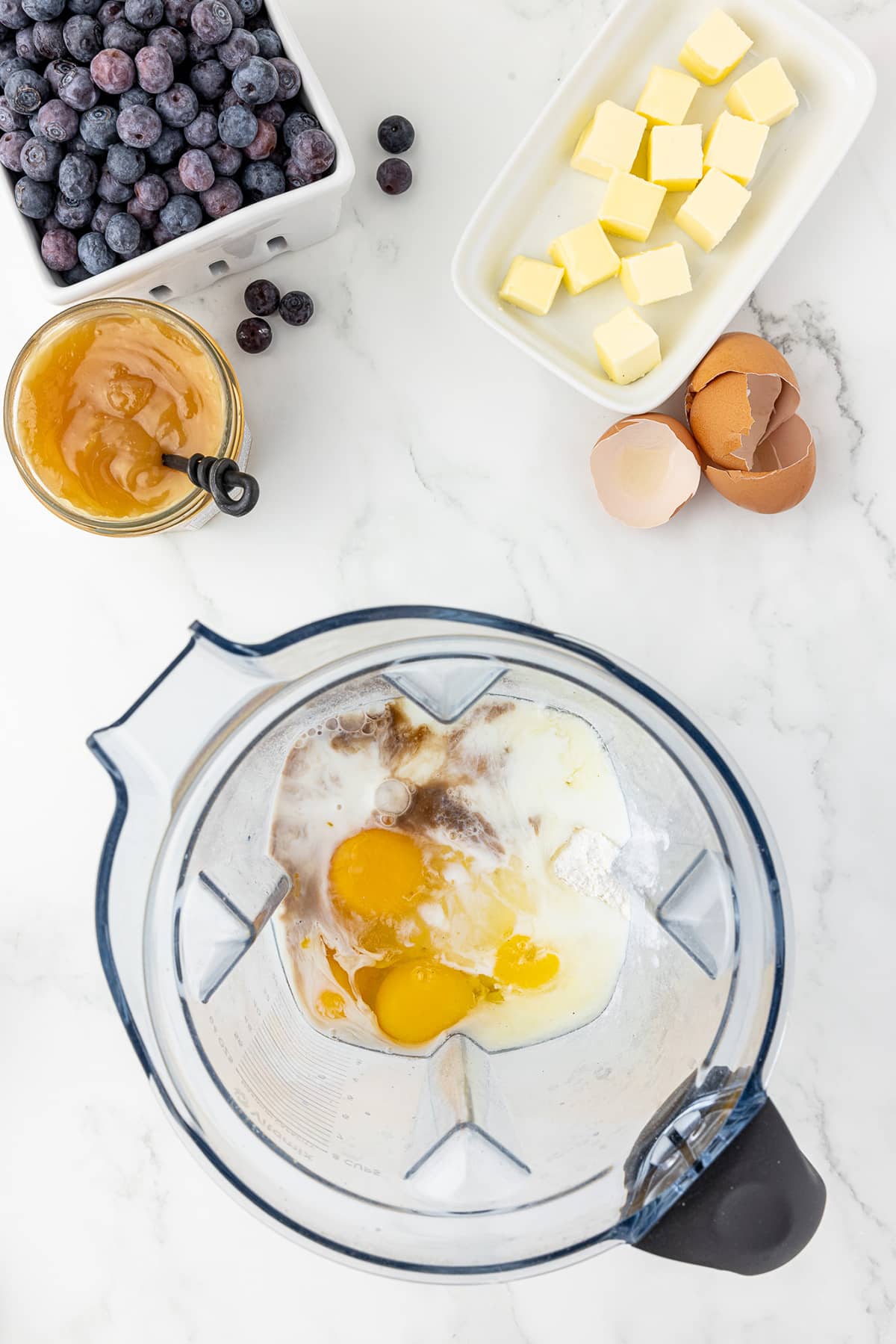 ingredients for pancake batter in a blender, blueberries, lemon curd, and cubes of butter