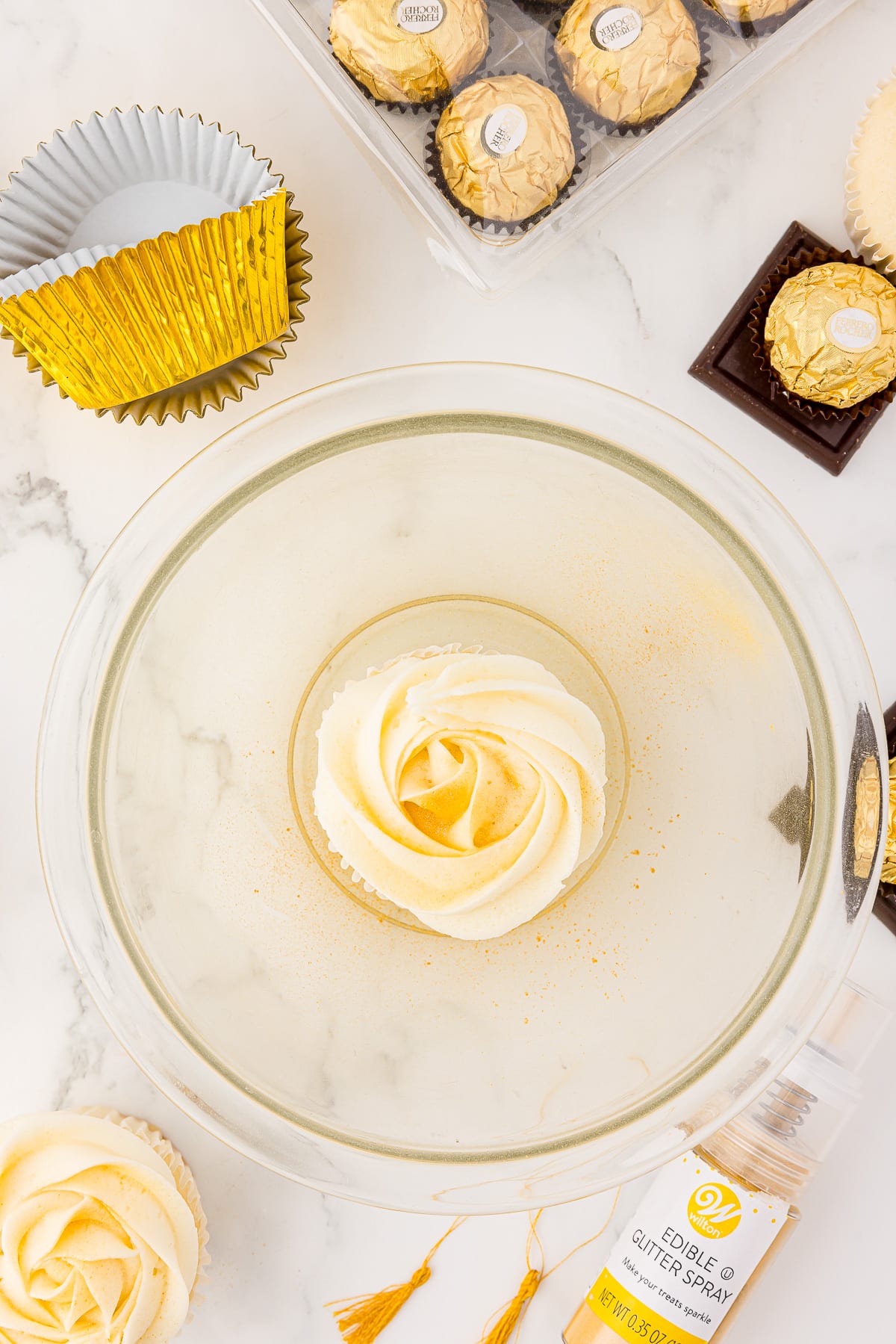 A cupcake in a bowl being sprayed with Wilton gold edible glitter spray