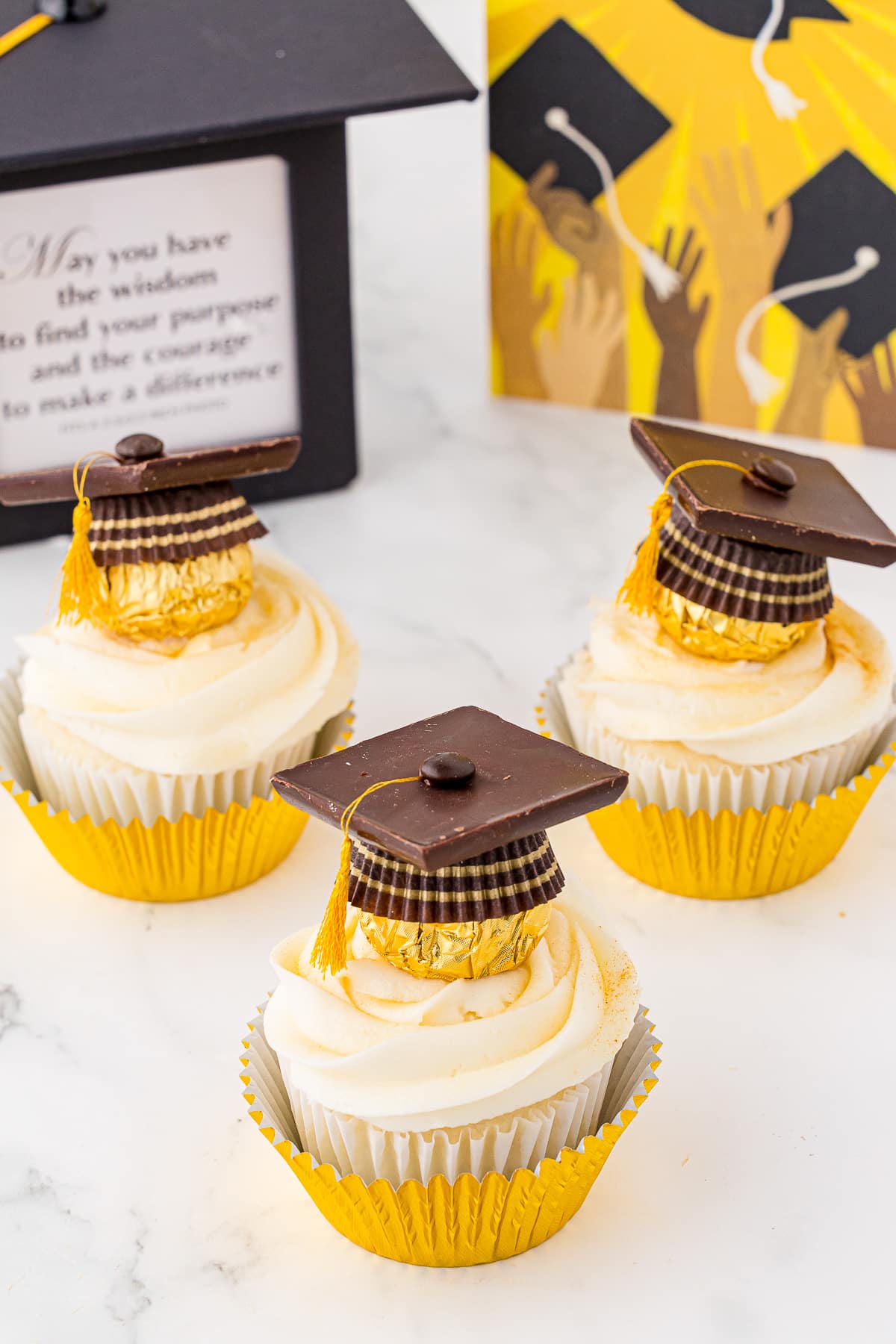 Graduation themed cupcakes with chocolate hats and gold foil wrappers with grad themed background