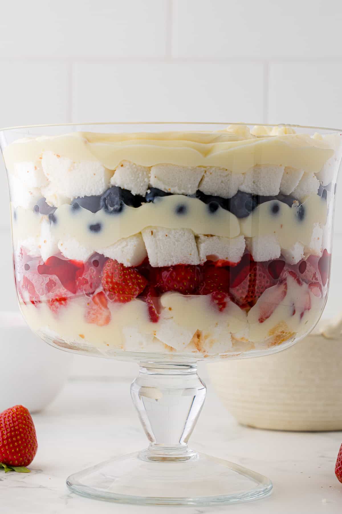 Side view of layered trifle in a glass bowl with layers of strawberries, blueberries, Cool Whip, and bite sized angel food cake pieces