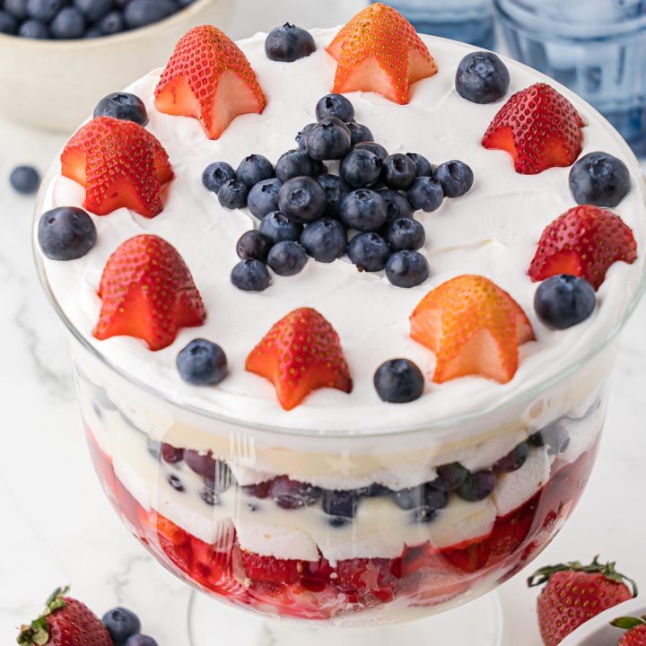 Star shaped strawberries and blueberries forming a star on top of strawberry and blueberry layered trifle in a glass bowl