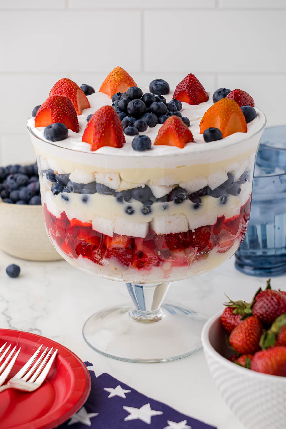 Strawberry, blueberry and cool whip layered trifle in glass bowl with patriotic napkins and plates
