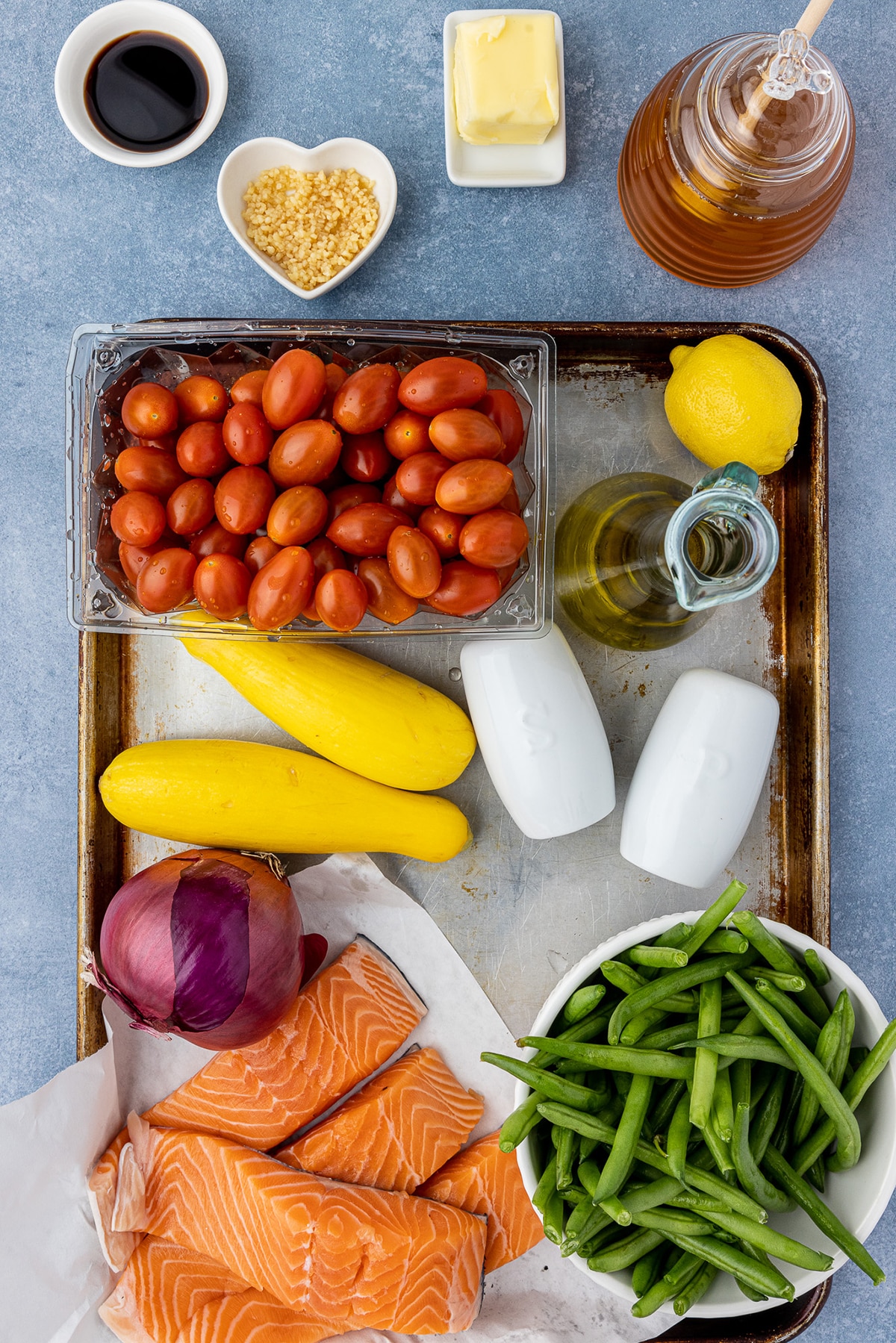 Ingredients for Sheet Pan Salmon with rainbow veggies on a blue countertop. 