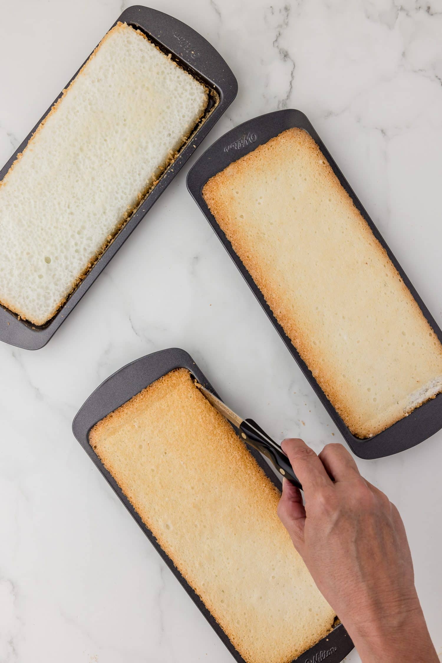 Running a knife around the edge of a loaf pan filled with baked angel food cake.