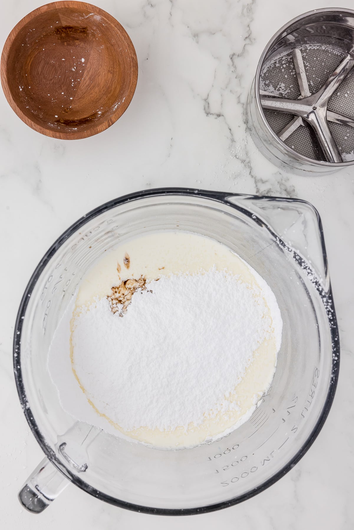 Batter bowl with cream, vanilla, and powdered sugar on a white counter top.
