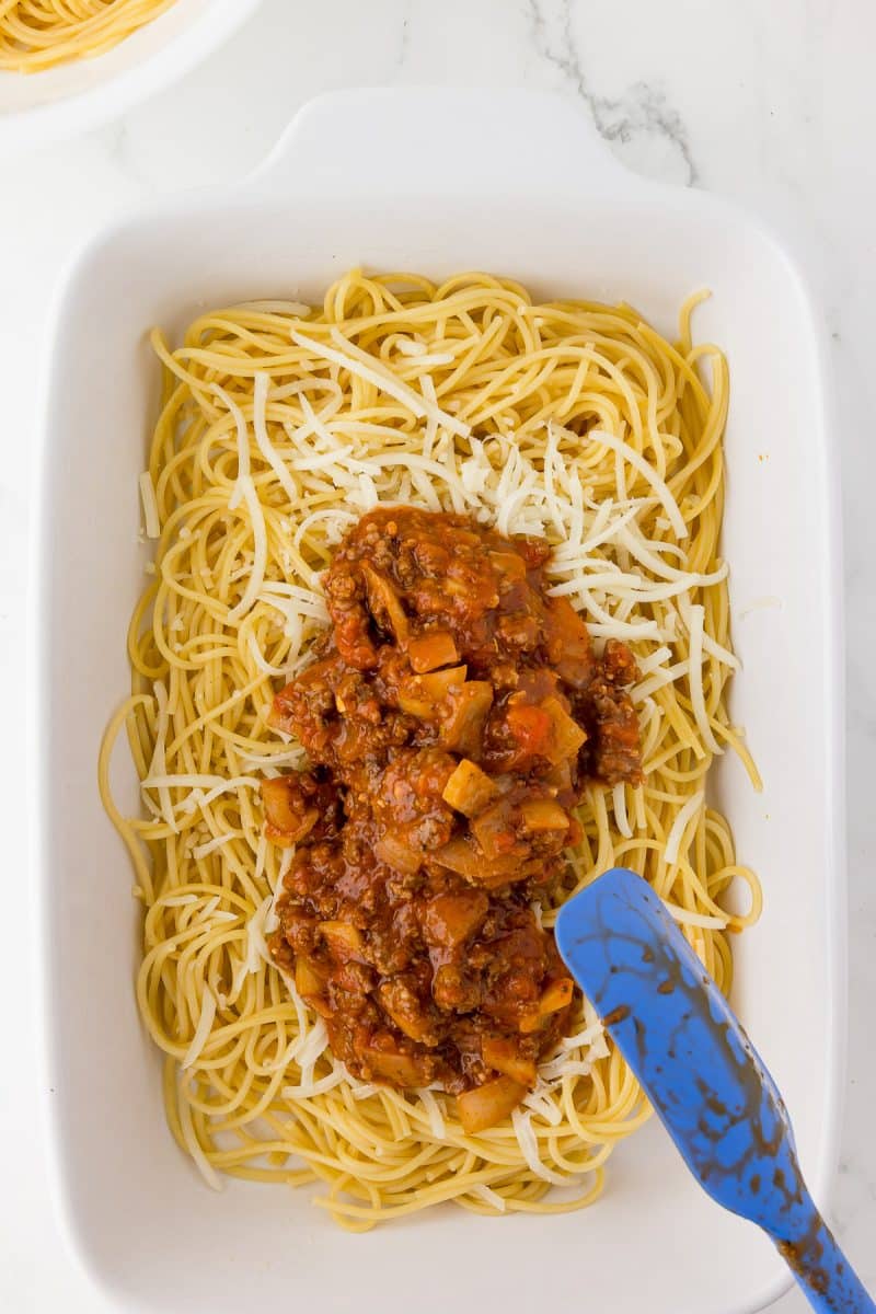 white baking dish with spaghetti, grated mozzarella and a scoop of meat sauce