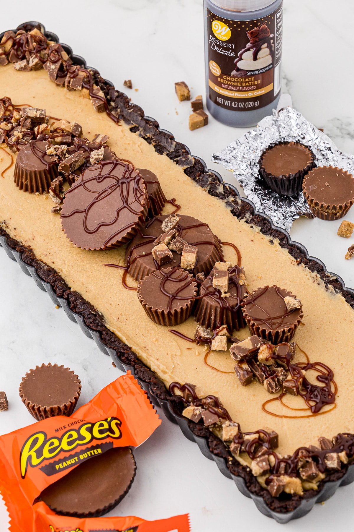 No bake peanut butter tart in a tart pan with wilton drizzle and reese's peanut butter cups
