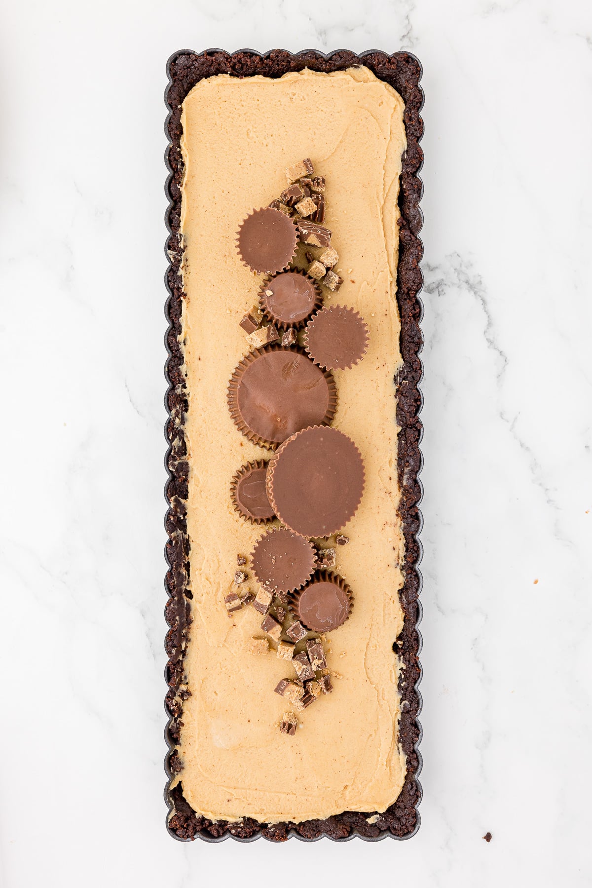 rectangle peanut butter tart with a brownie curst and topped with peanut butter cups white marble countertop