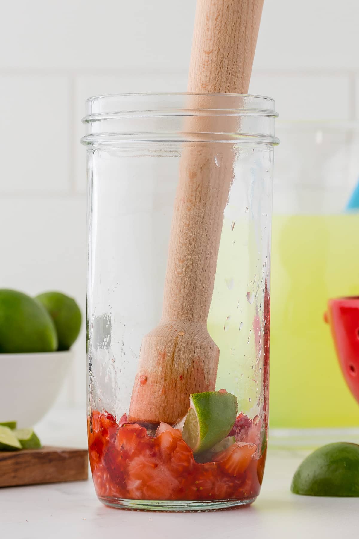 Strawberries and limes being mashed in the bottom of a clear glass jar