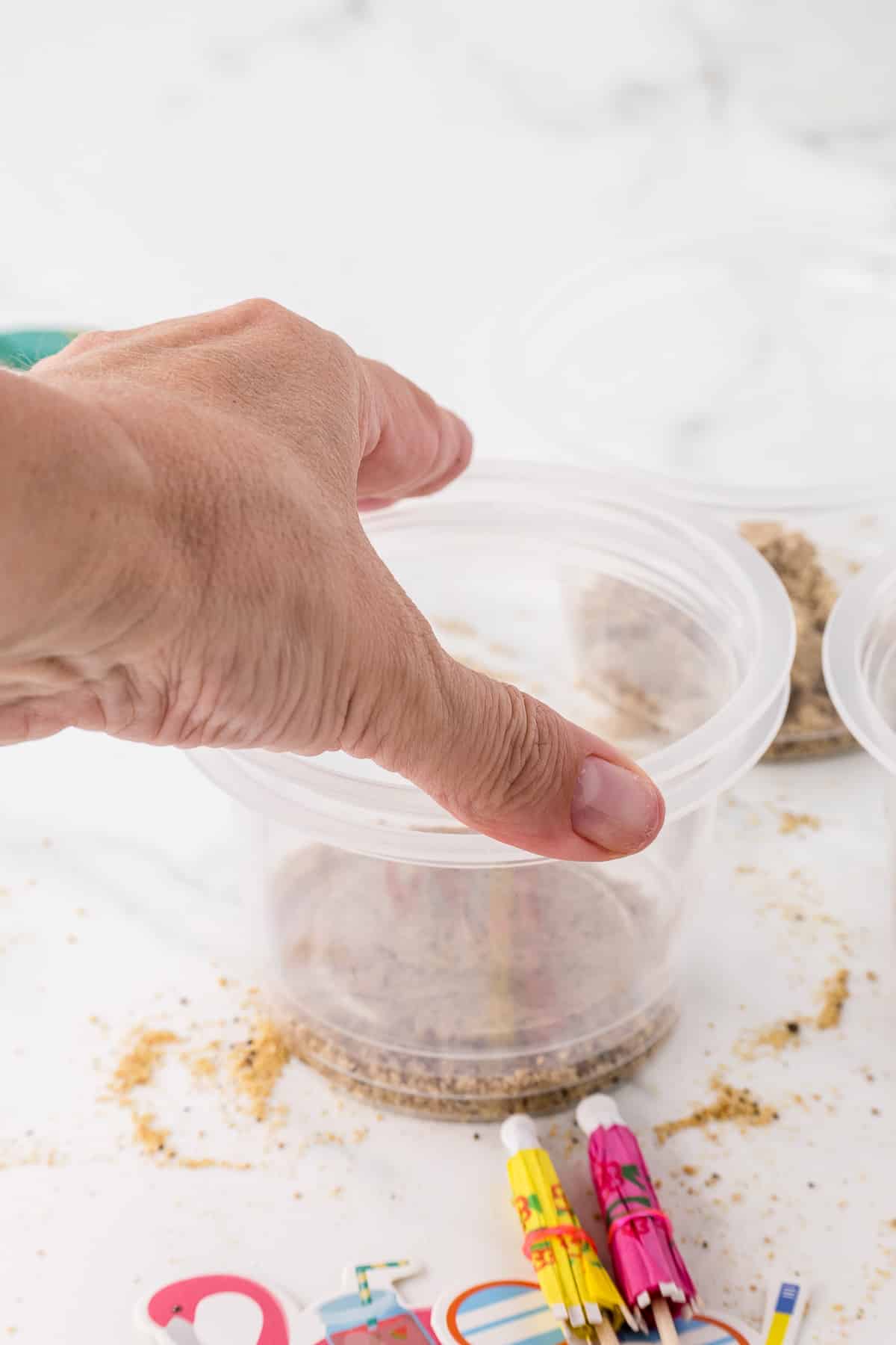 a hand using a clear cup to press another cup down onto edible sand at the bottom