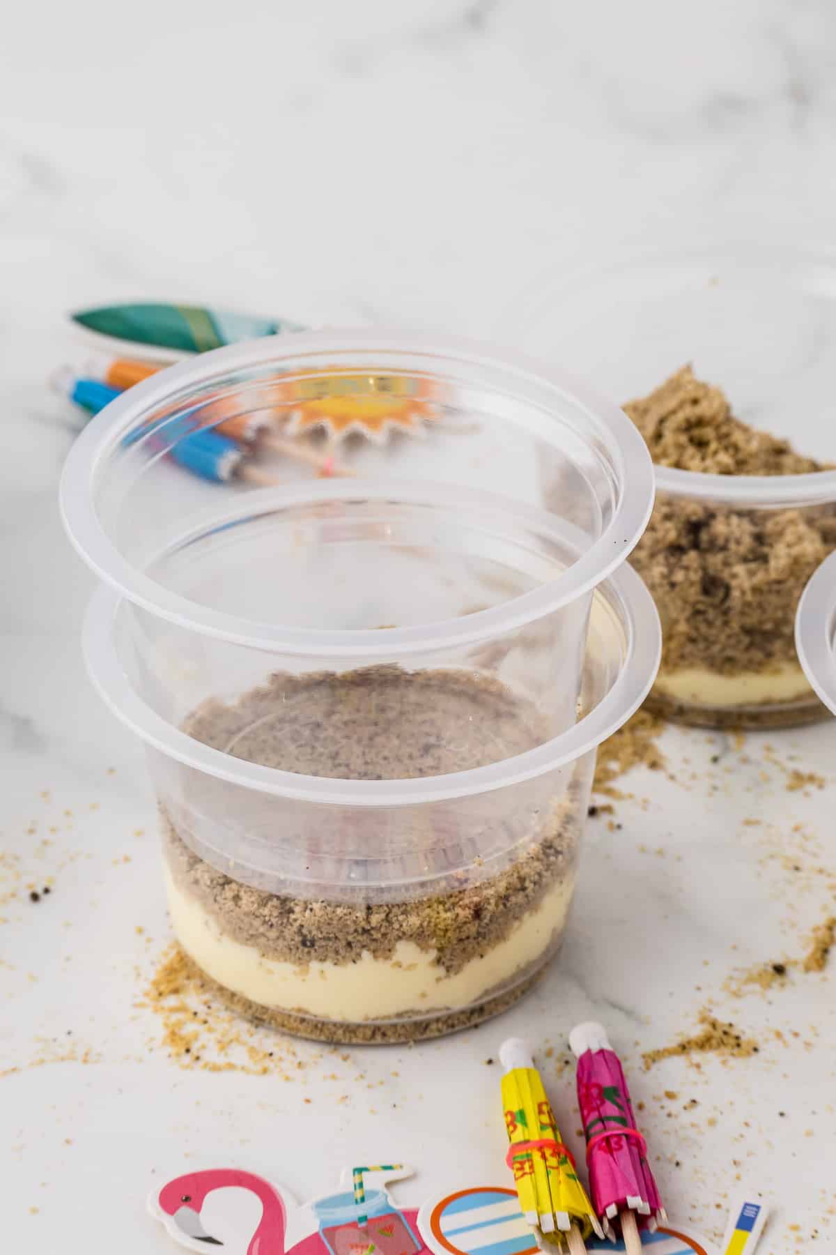 Two clear plastic cups pressed together to smash the cookie crumbs down into the pudding to make sand pail treats.