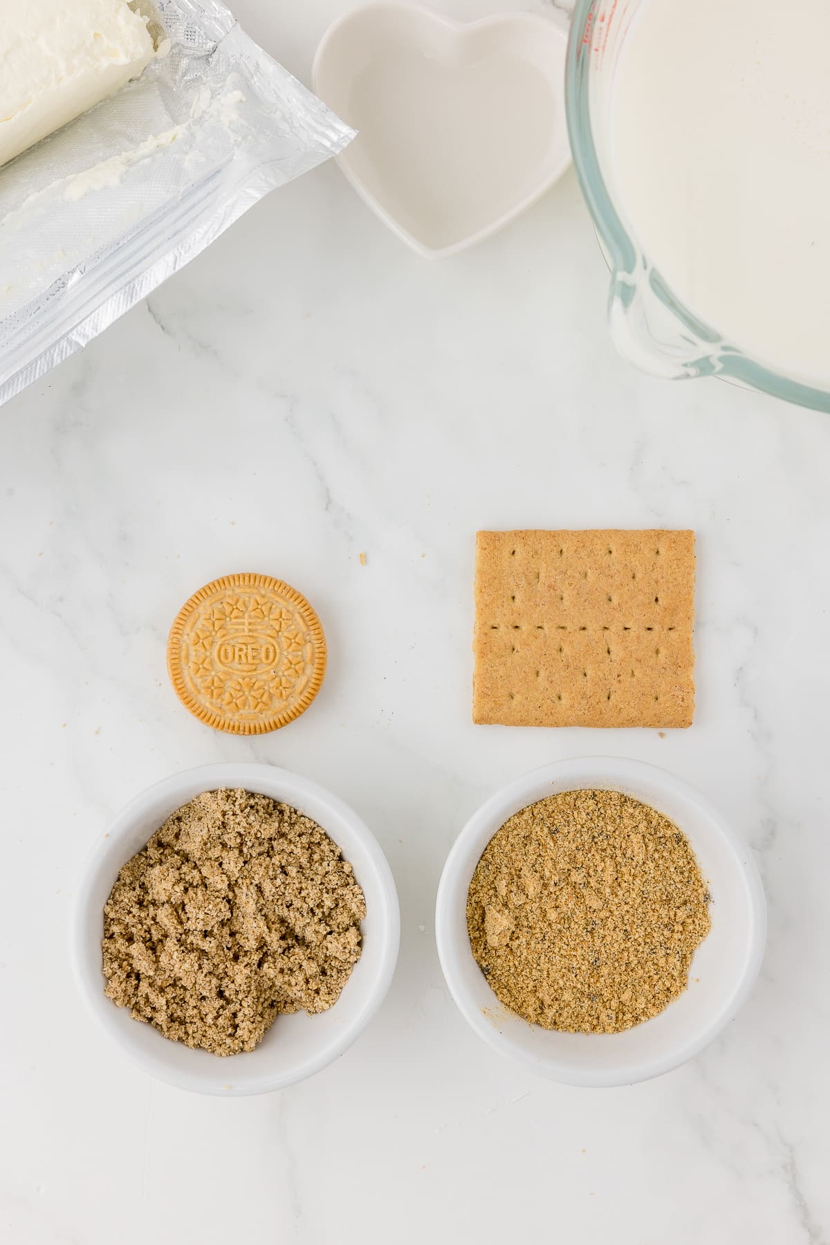 a bowl of crumbed golden oreo cookie and a bowl of crumbled graham cracker on a white marble counter.