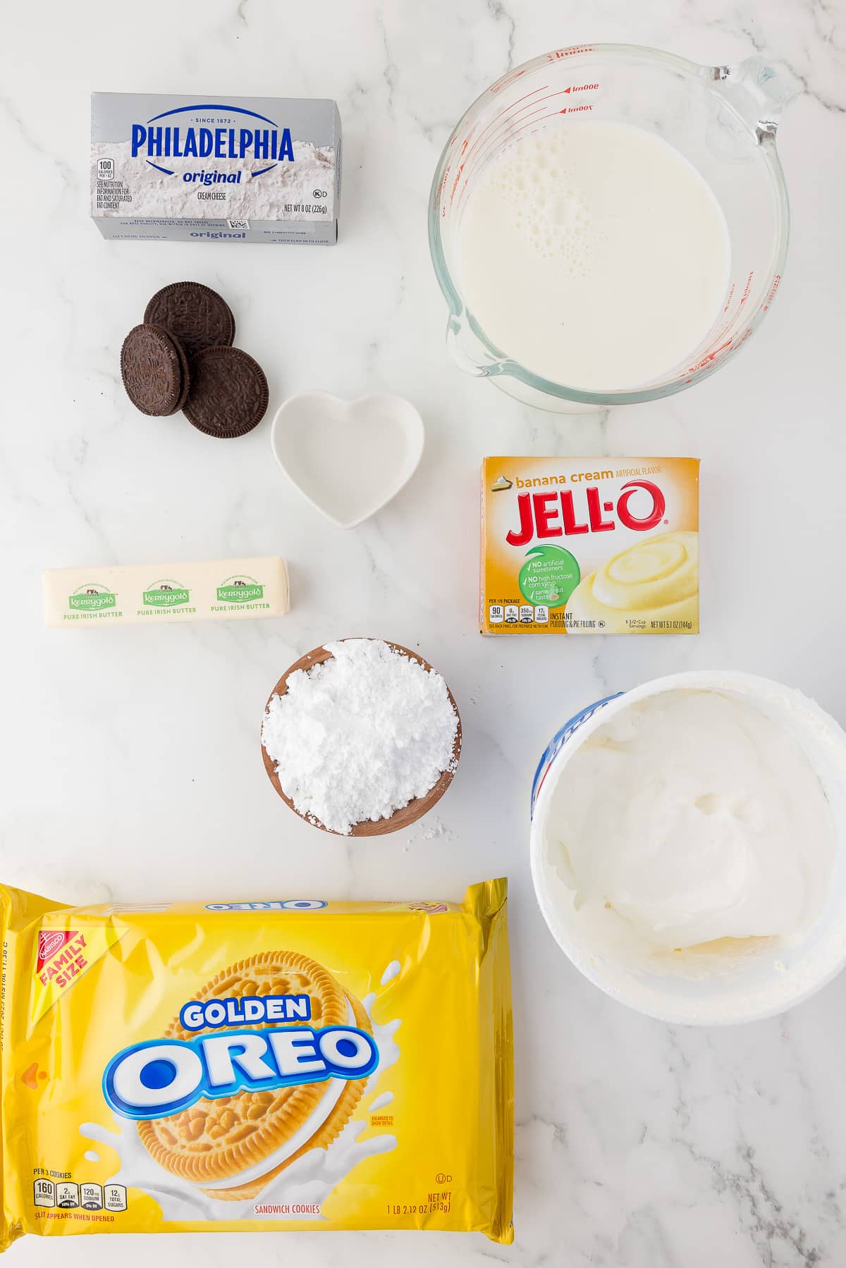 A box of golden oreo cookies, jell-O pudding mix, powered sugar, cream cheese on a marble white counter top.