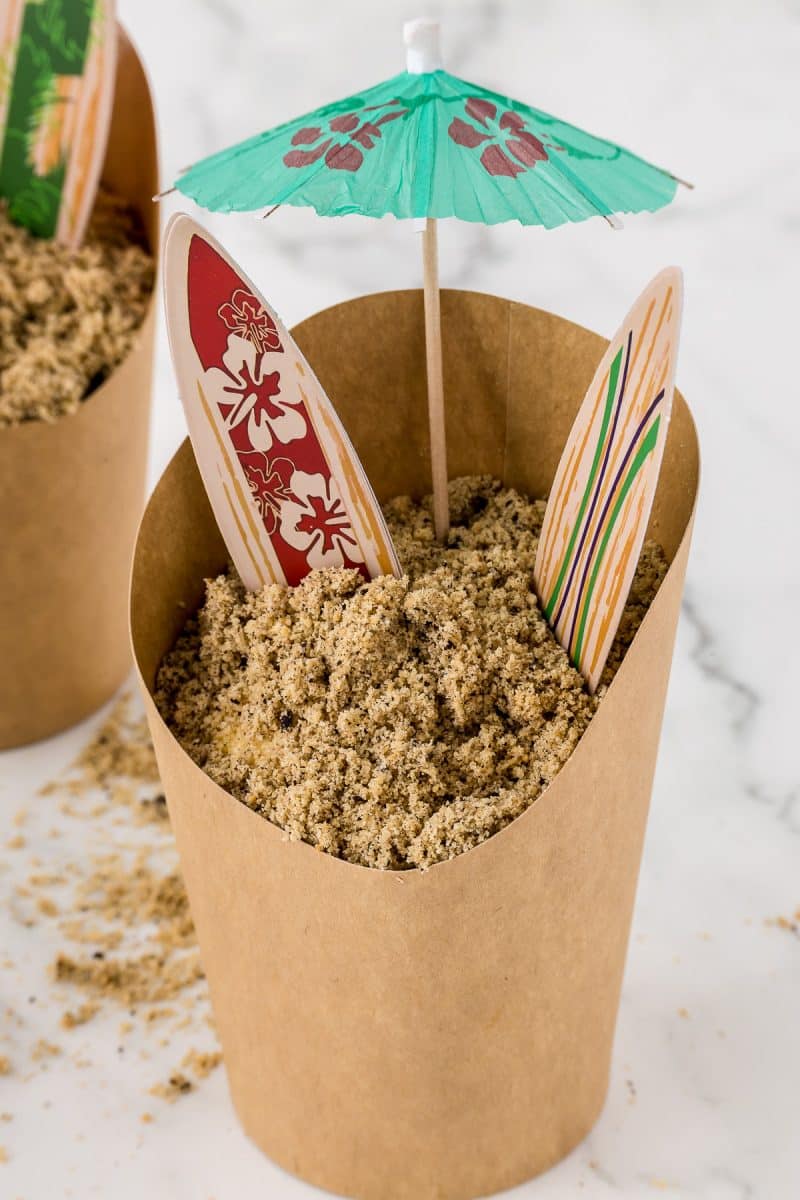 Sand pudding dessert idea for a beach themed party with surf boards and a paper umbrella.