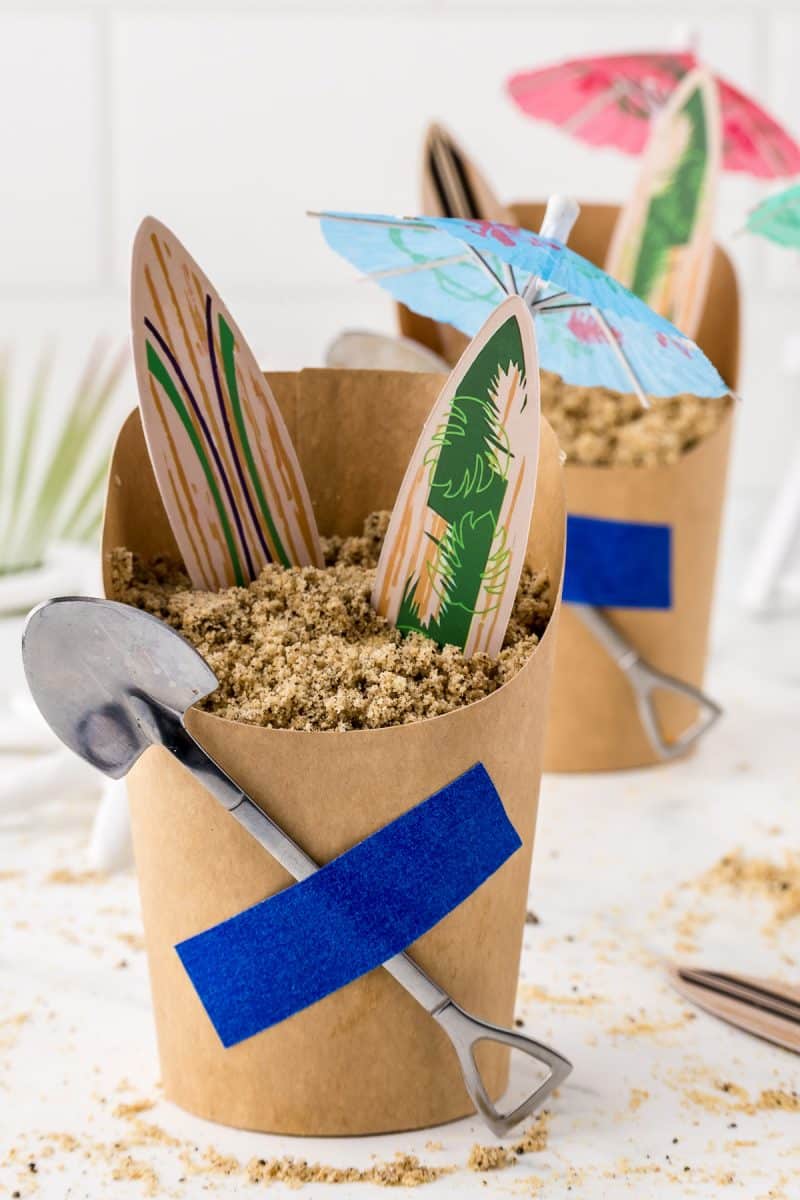 A beach themed sand pudding dessert with surf boards and paper umbrella.