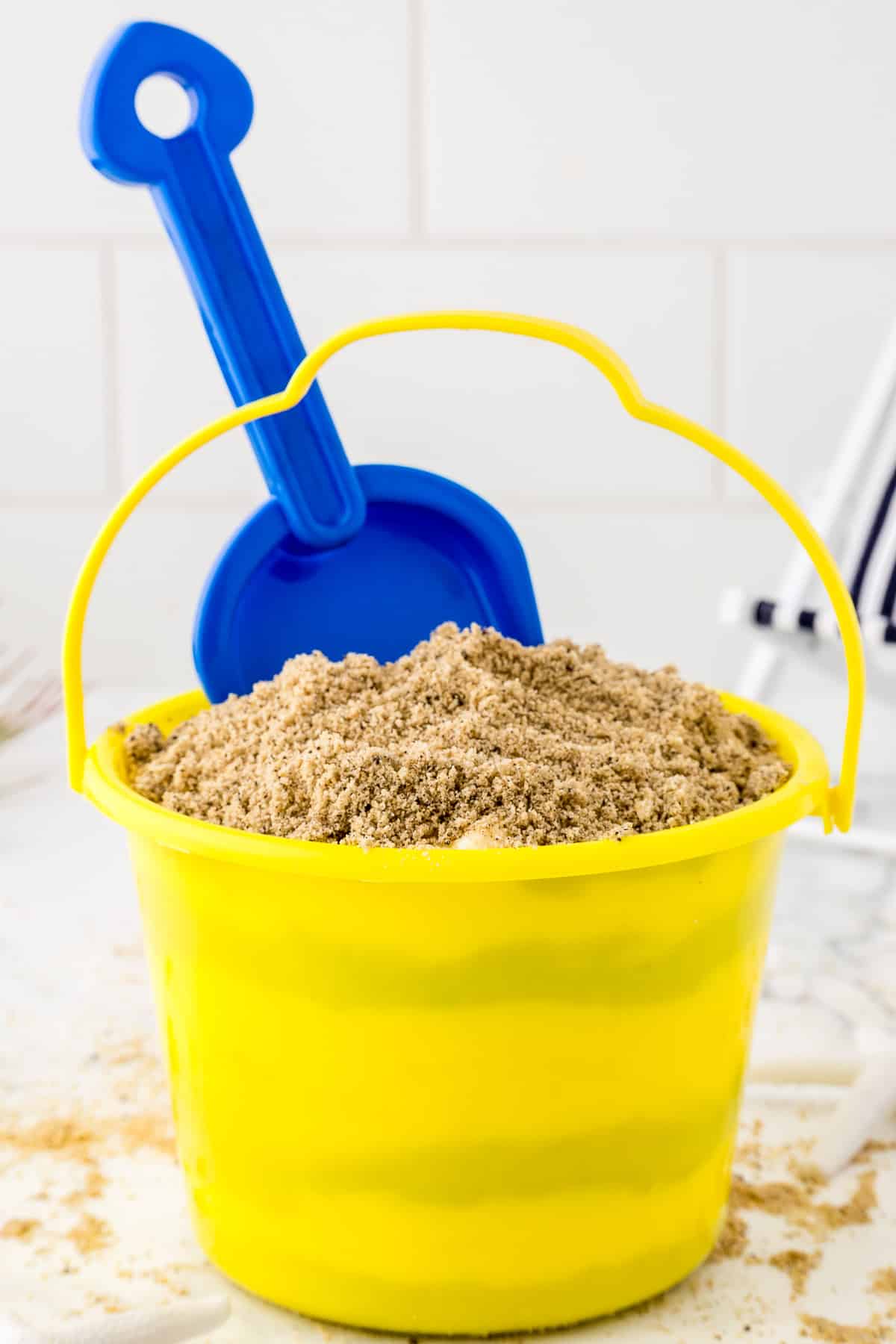 Yellow sand bucket full of sand cookie crumbs with a blue sand shovel.
