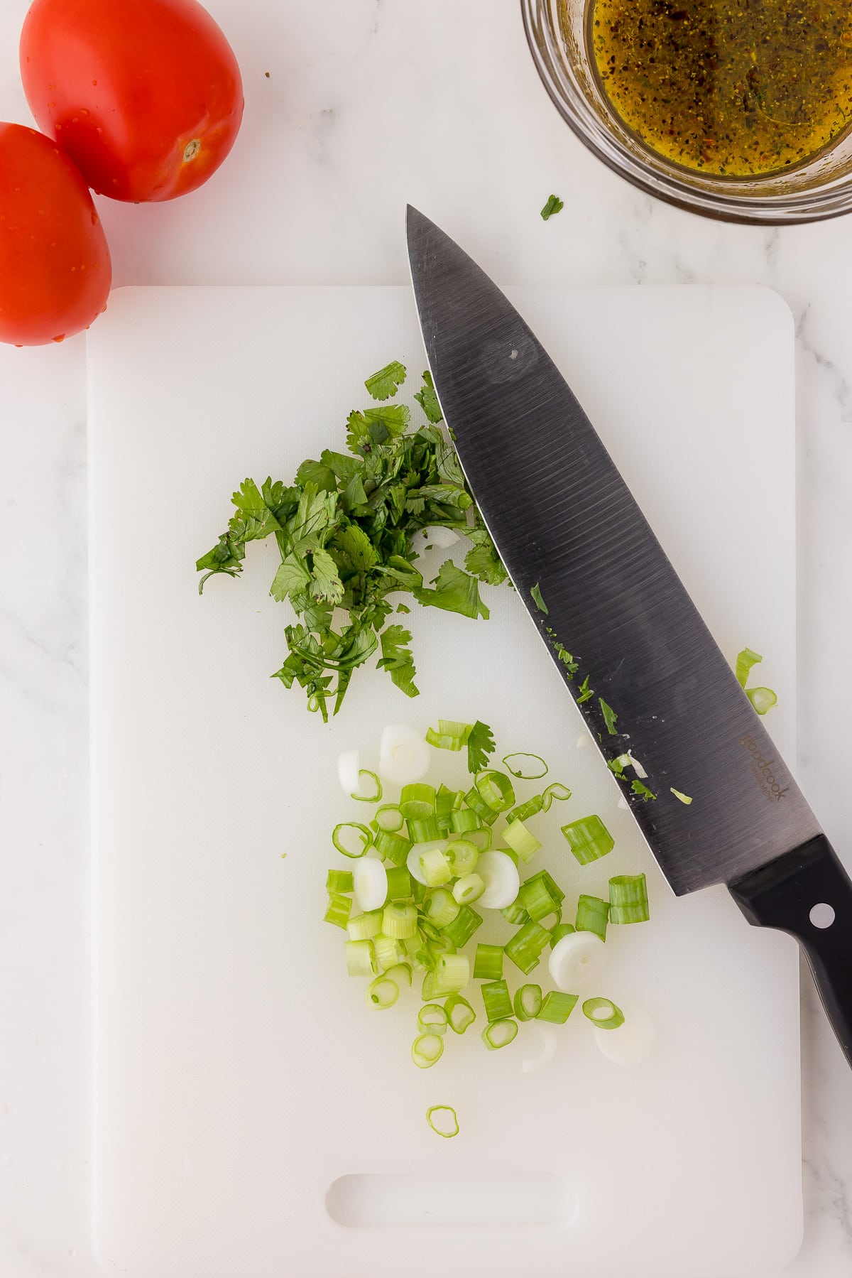 A large knife resting on a white cutting board with green onions and cilantro