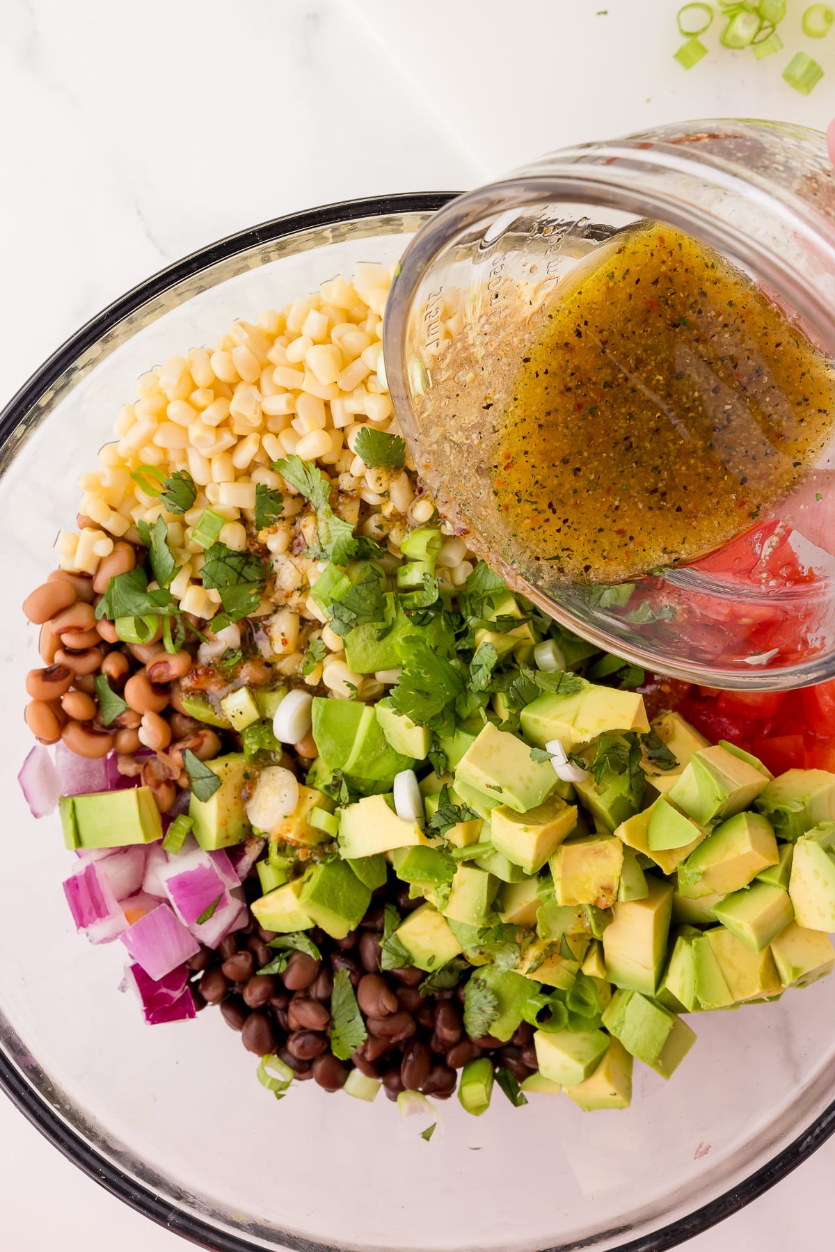 Bowl full of beans, avocado, corn and onions with dressing being poured on top