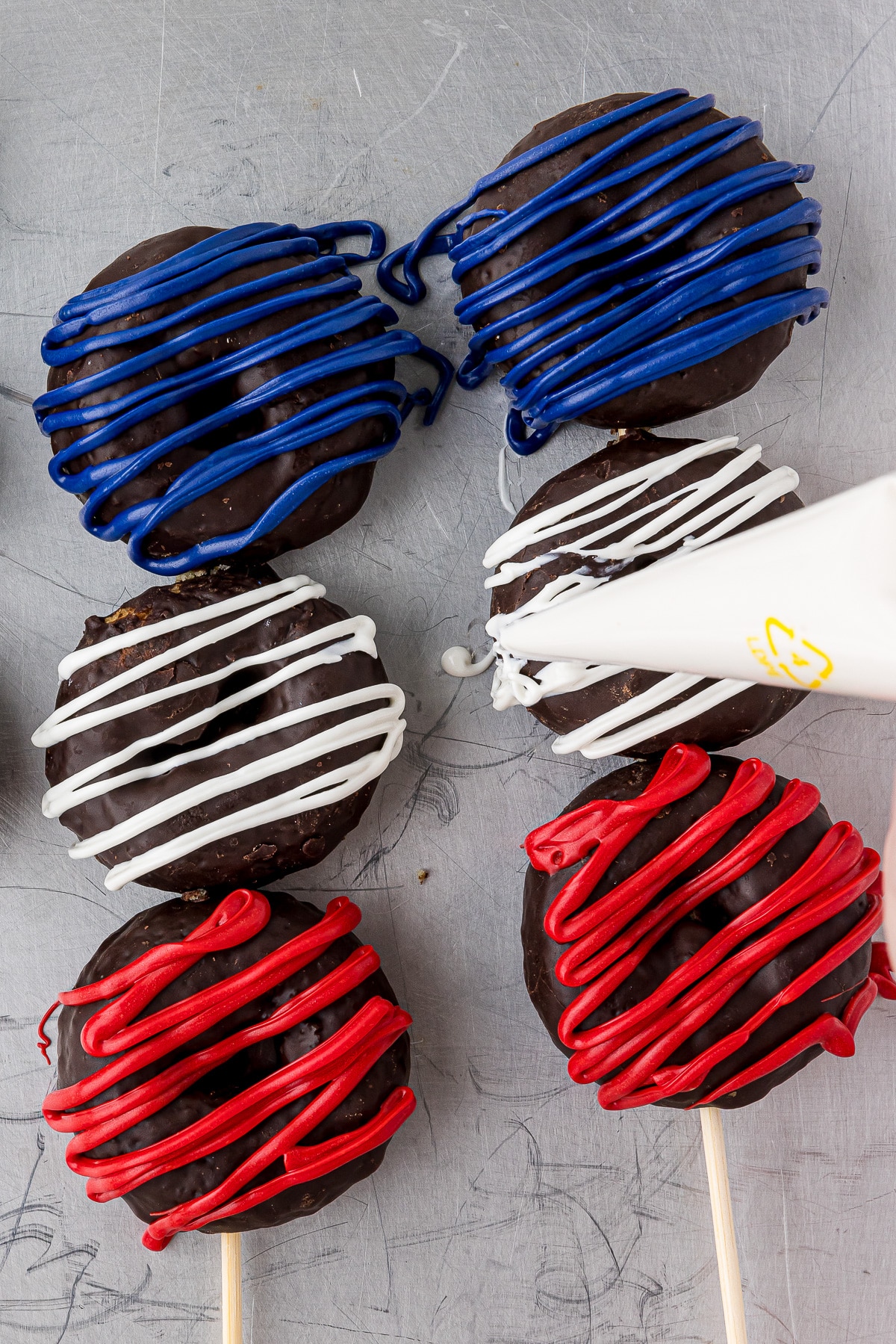two sets of three chocolate donuts on a skewer, decorated in red white and blue decorating chocolate.