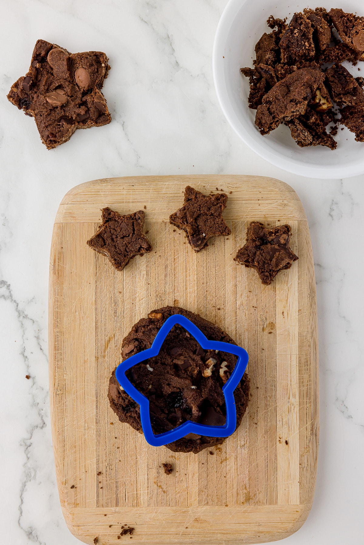 baked chocolate walnut cookies being cut into star shapes on a light cutting board.