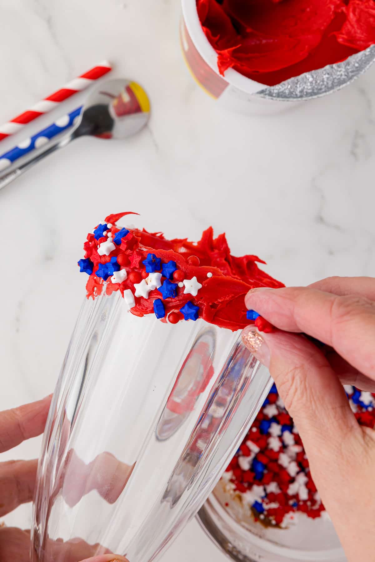 shake glass whose rim is frosted with red frosting, white and blue small candy stars being applied