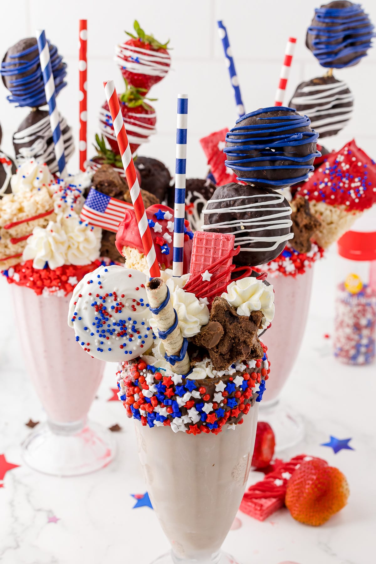 two strawberry and one chocolate milkshakes decorated with red white and blue cookies